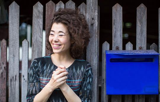 smiling woman standing near the fence with a blue mailbox