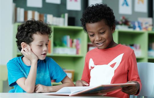 two boys smiling, reading and studying together in their classroom