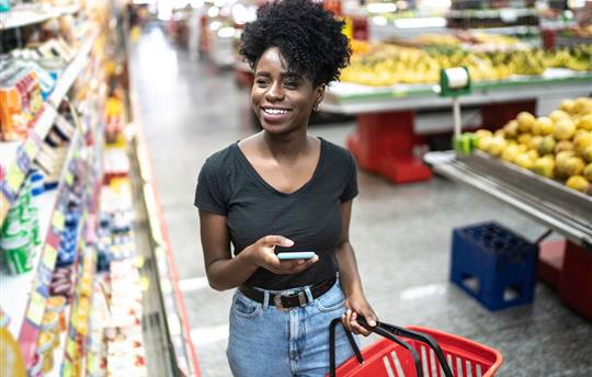 Young woman using mobile phone and choosing product in supermarket