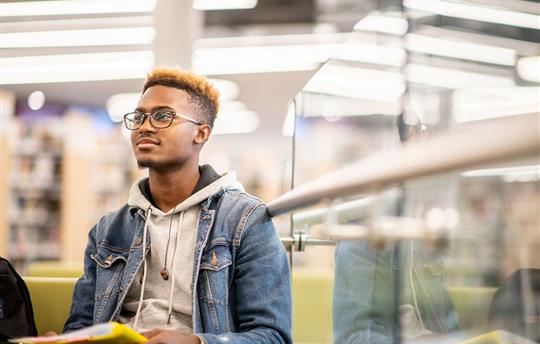 college student in denim jacket over a gray hooded sweatshirt in library