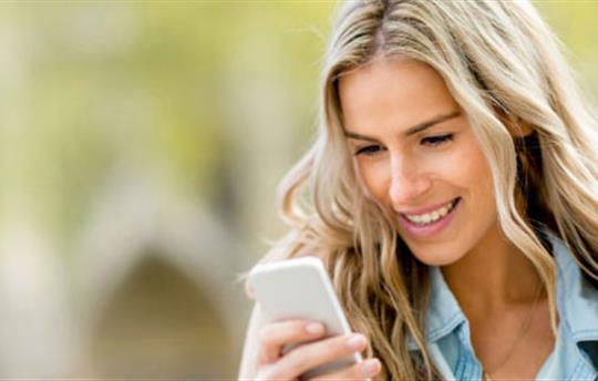 woman with blonde hair smiling as she looks at her smartphone