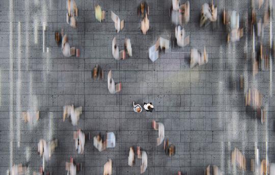birds-eye view of two, still people on the street with other people walking by