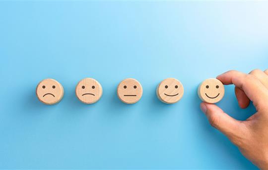 Customer satisfaction survey concepts. The client's hand picked the happy face smile face icon on wooden cube on blue background.